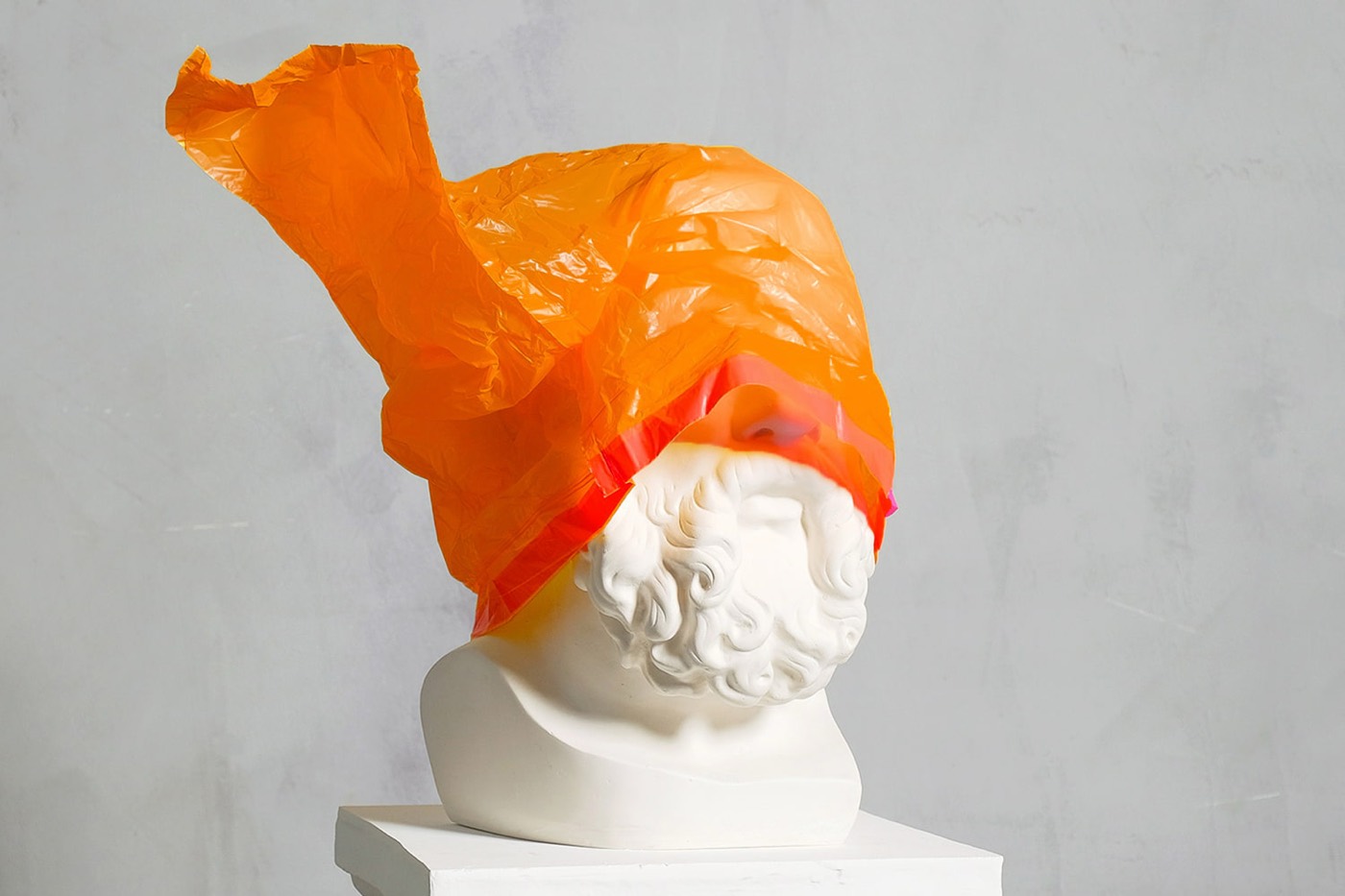 Classical plaster bust wearing a bright orange plastic bag — creative direction by José Rocha