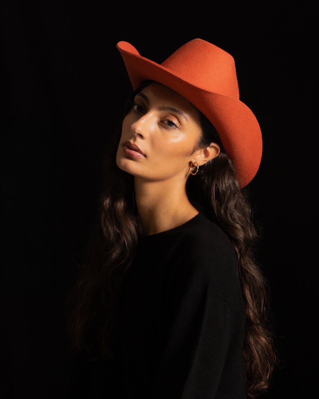 Studio portrait against black — terracotta hat, three-quarter turn