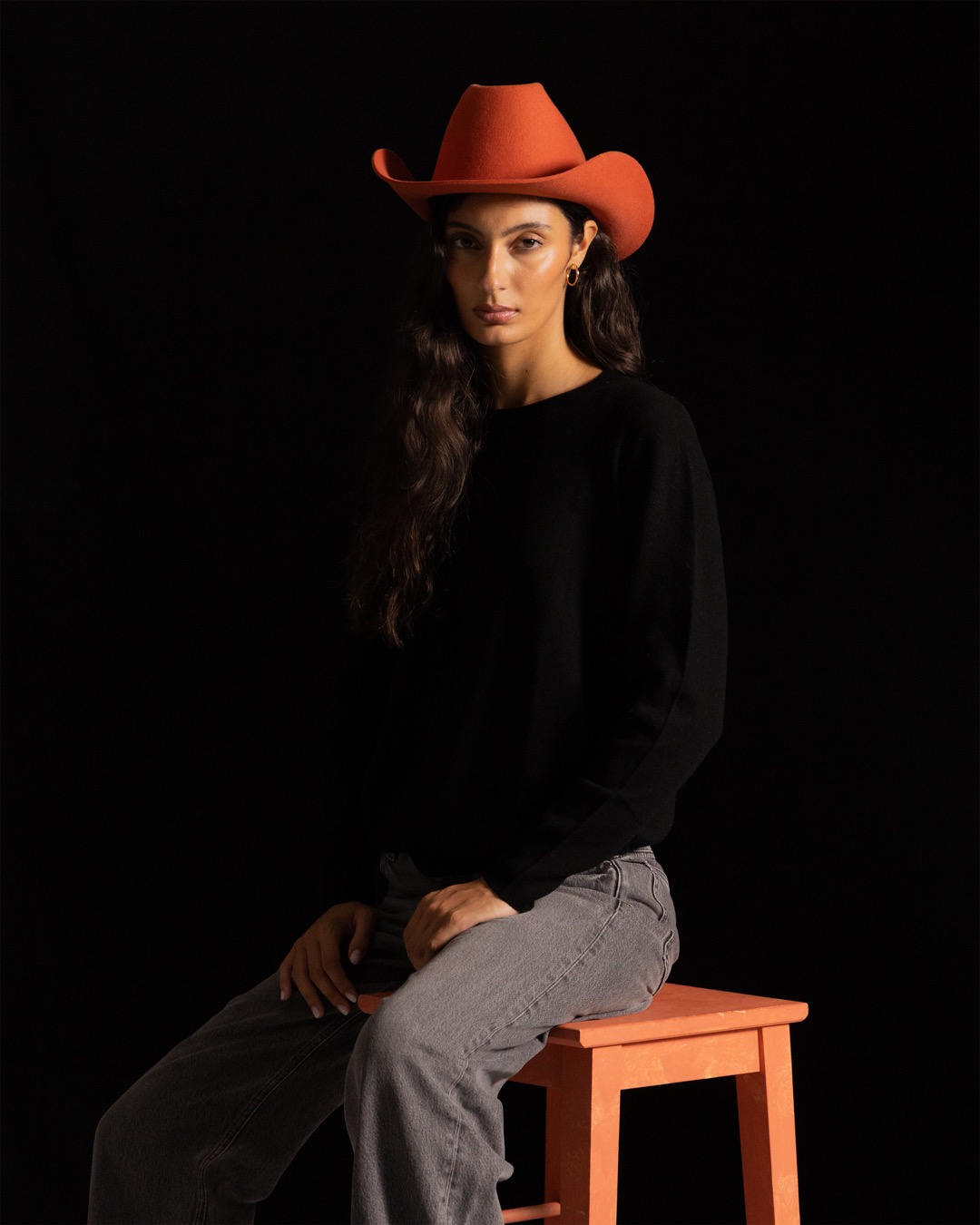 Studio portrait against black — seated on a terracotta stool